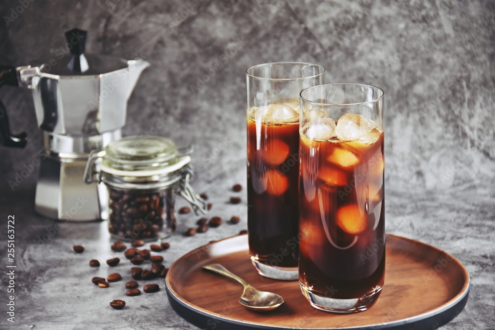 Ice coffee in a tall glass with cream poured over and coffee beans on a old rustic wooden board. Cold summer drink on a dark wooden background with copy space Ice coffee in a tall glass with cream poured over and coffee beans on a old rustic wooden board. Cold summer drink on a dark wooden background with copy space