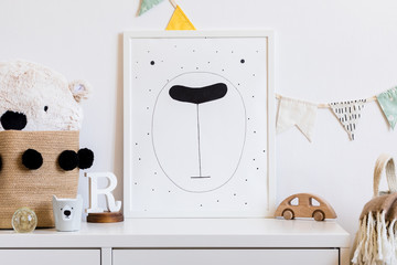 Stylish scandinavian newborn baby room with toys, teddy bear, cotton flags and natural basket. Modern interior with mock up photo or poster frame. Real photo. Template.
