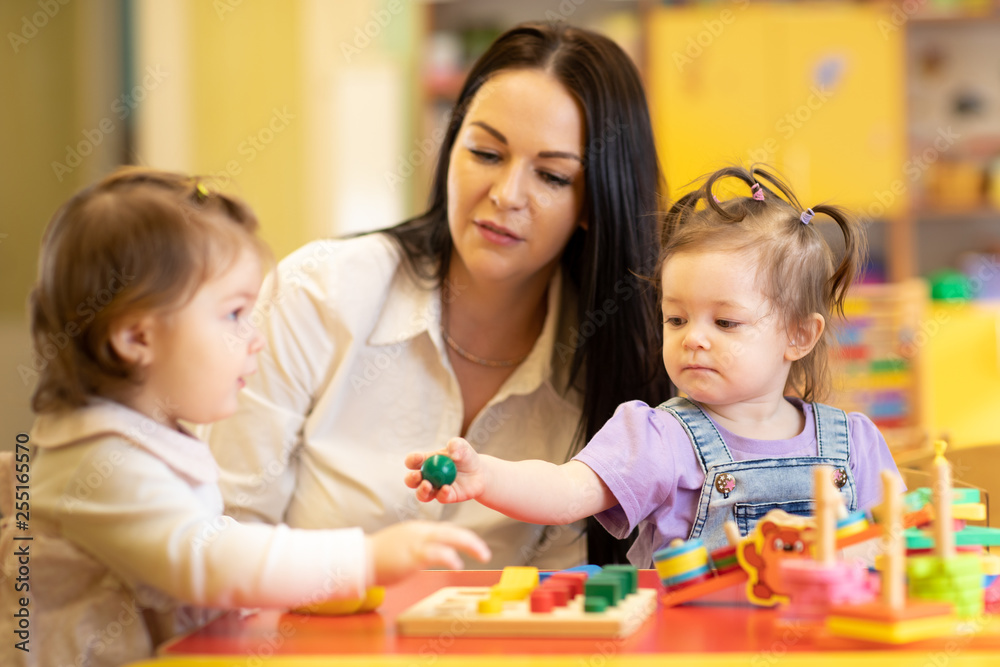 Nursery babies group playing with teacher in daycare centre playroom