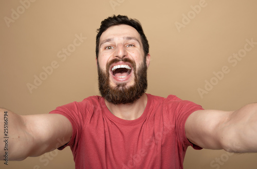 Close up photo of beautiful amazing bearded brunet he him his handsome hold telephone in arms make take selfie wear casual checkered plaid t-shirt outfit isolated on beige background