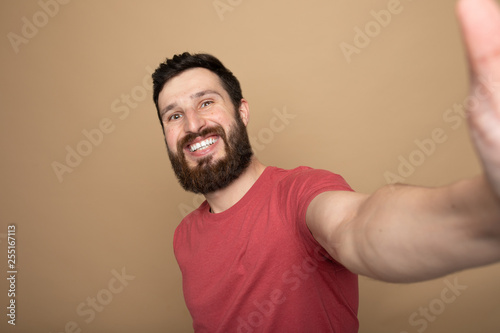 Close up photo of beautiful amazing bearded brunet he him his handsome hold telephone in arms make take selfie wear casual checkered plaid t-shirt outfit isolated on beige background