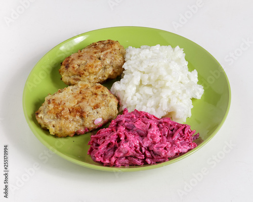 Cutlets, boiled rice and chopped beets on a plate on a white background.