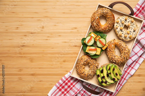 Stylish and tasty composition of vegan bagels sandwiches on the salver with vegetables, herbs, paste, seeds, hummus and lettuce on the brown wooden table. Fresh and healthy breakfast. Copy space.