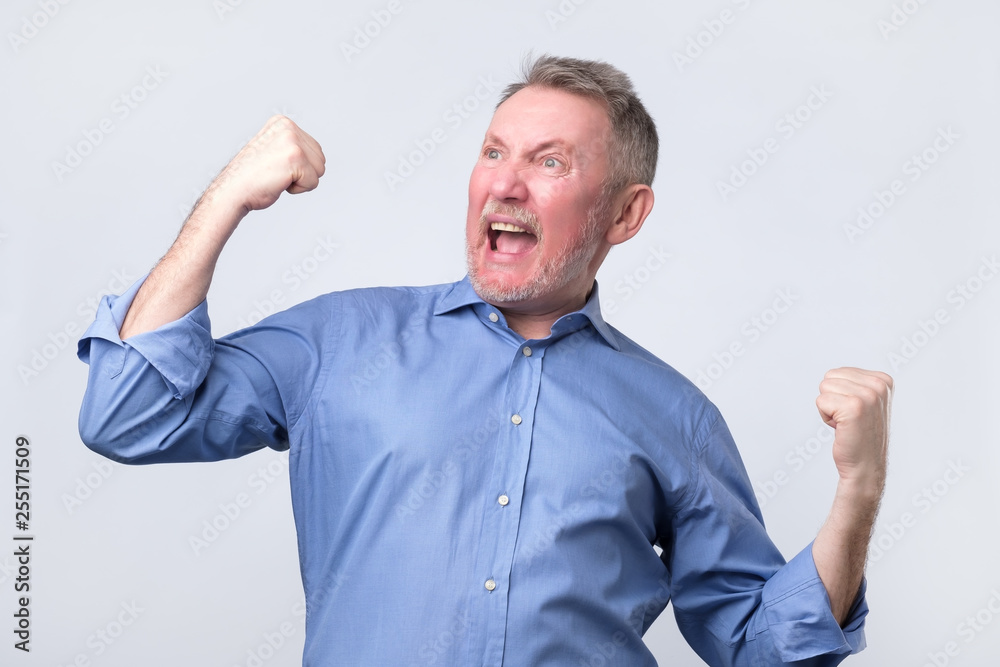 Happy senior strong man, raising clenched fists in hooray gesture, triumphing Happy senior strong man, raising clenched fists in hooray gesture, triumphing