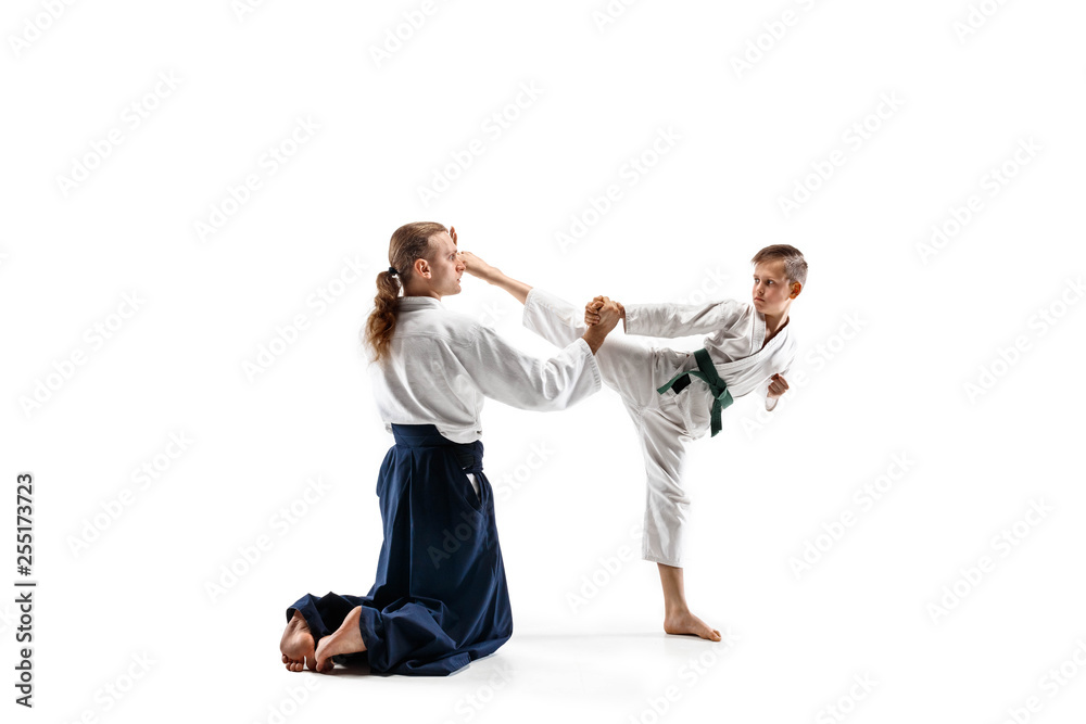 Man and teen boy fighting at Aikido training in martial arts school. Healthy lifestyle and sports concept. Fightrers in white kimono on white background. Karate men with concentrated faces in uniform. Man and teen boy fighting at Aikido training in martial arts school. Healthy lifestyle and sports concept. Fightrers in white kimono on white background. Karate men with concentrated faces in uniform.
