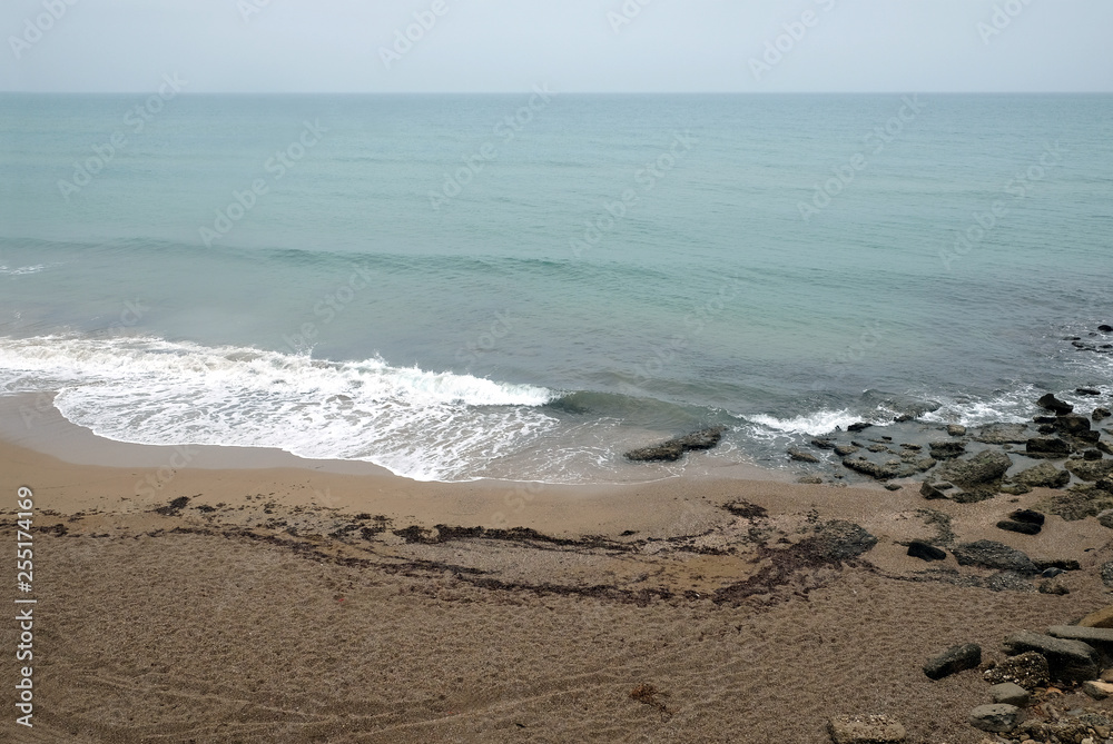 Seascape with empty sandy beach and sea surf with foamed waves on overcast day on resort in low season top view