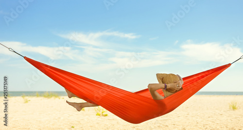 Relaxed woman lying in a hammock with the view of blue sky and sea line