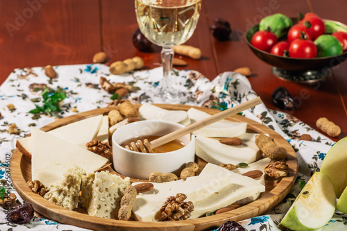 Assorted cheeses on round wooden board plate served with white wine Guda cheese, cheese grated bark of oak, hard cheese slices, walnuts, grapes, crackers, honey, sulguni, light wood background