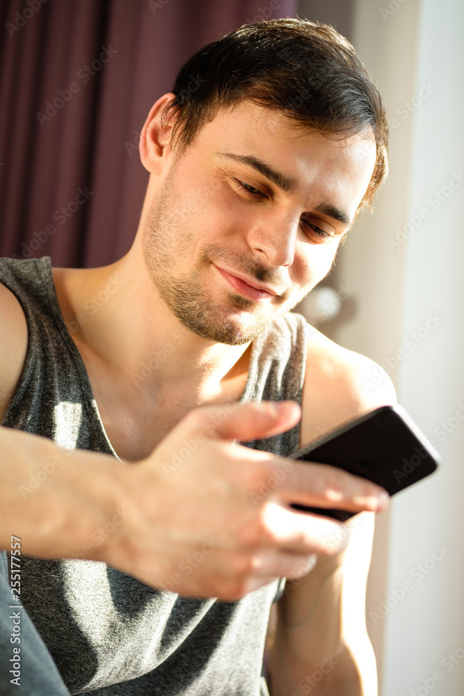 Young handsome man using phone while having exercise break in gym. Guy using smartphone after the daily training. Young handsome man using phone while having exercise break in gym. Guy using smartphone after the daily training.