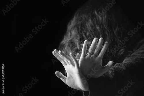 Violence against women. Black and white portrait of scared and desperate woman, focus on the hands in protective gesture