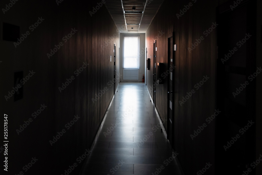 Dark corridor with doors and window light in the end