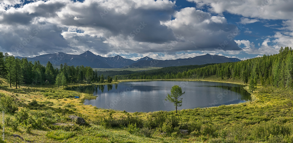 Fototapeta premium tourism and travel, summer landscape in Altai mountains, round small lake. white clouds in the blue sky are reflected in the water.