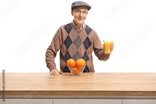 Senior man holding a glass of orange juice behind a wooden counter
