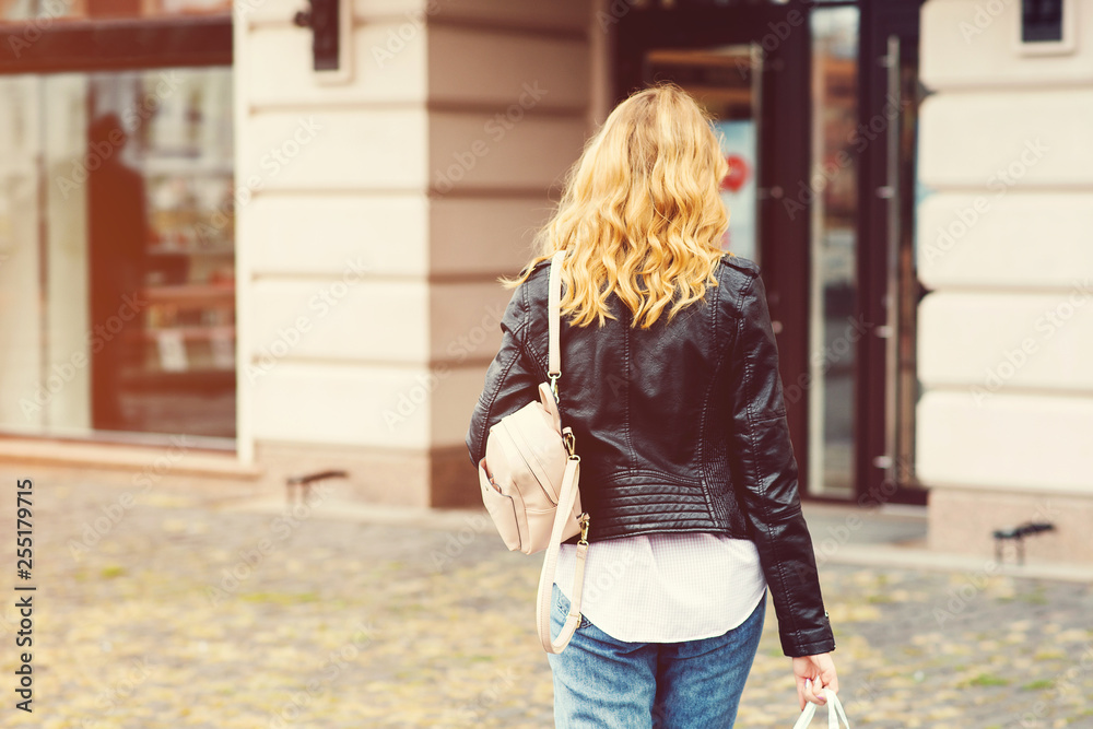 Stylish woman going to shopping. Consumerism, shopping, sales, lifestyle concept. Back view of happy woman with backpack. Urban girl enjoying city walk.