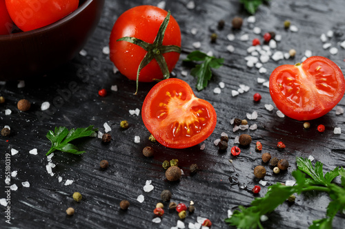 Fresh Sliced Cherry Tomatoes on a black background with spices coarse salt and herbs