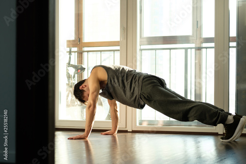 A handsome man doing plank exercises against the window of a house