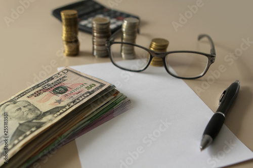 Euro and dollar banknotes, closeup lie on a white sheet of paper next to a pen on a light background and glasses in a plastic frame