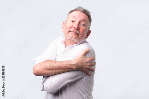 Smiling senior man holding hugging himself isolated on grey wall background.