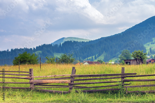 wooden fence in a meadow in the mountains, houses in the background