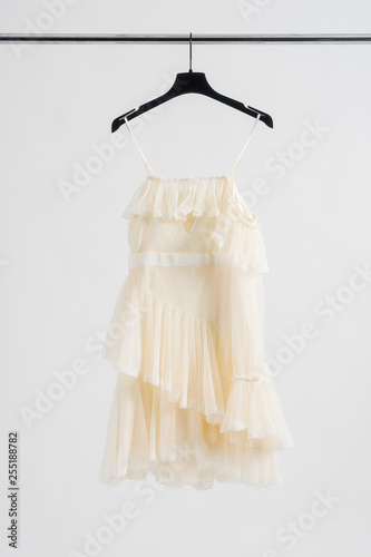 Beautiful white short wedding dress hanging on dressing rail. White background with copy space. Vertical photo.