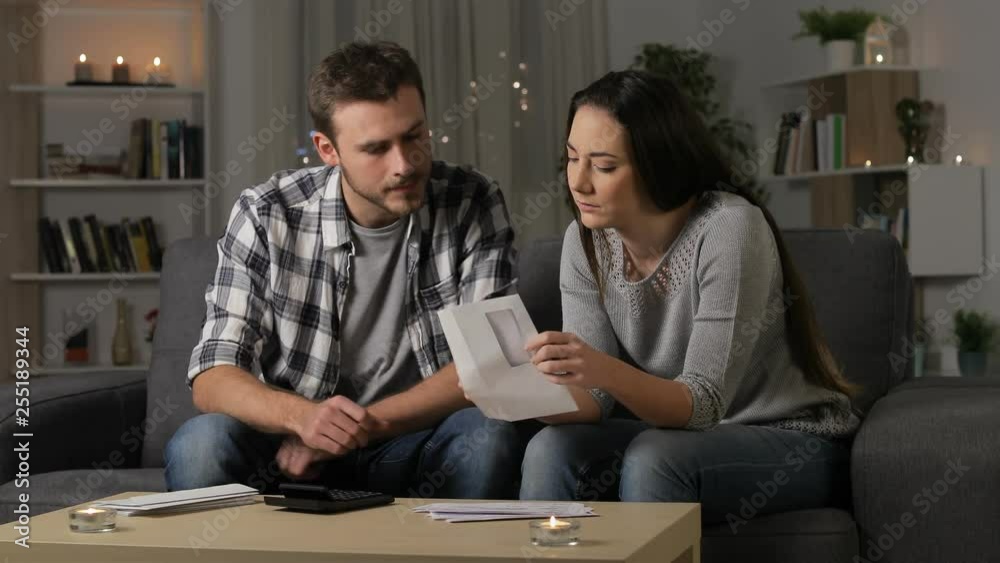 Confused couple reading receipts sitting on a couch in the night at home