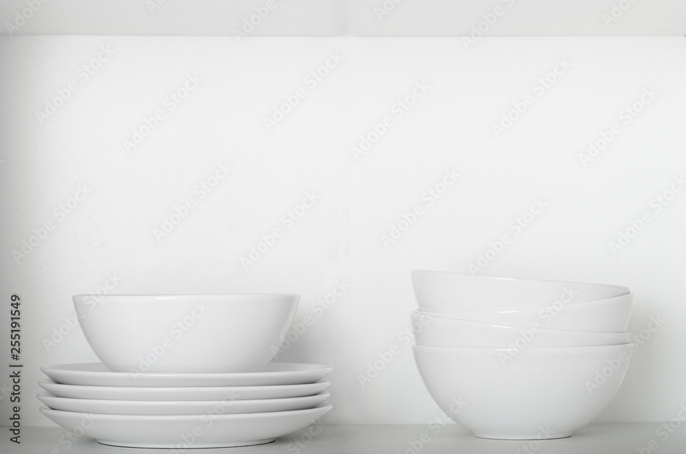 White plates and bowls on a shelf in the cupboard. Kitchenware, clean dishes