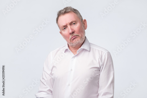 Old senior man in white shirt with serious and sad expression.