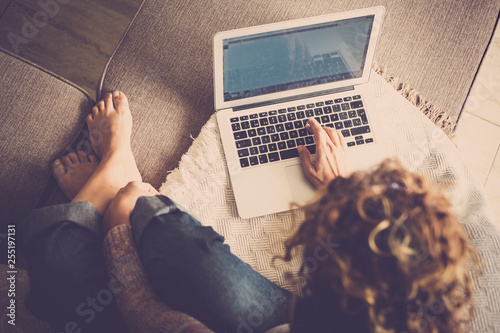 caucasian woman in casual clothes at home, barefoot and comfortable, type on a laptop working free and independent - alternative digitla nomad and frelance work style - viewed from above photo