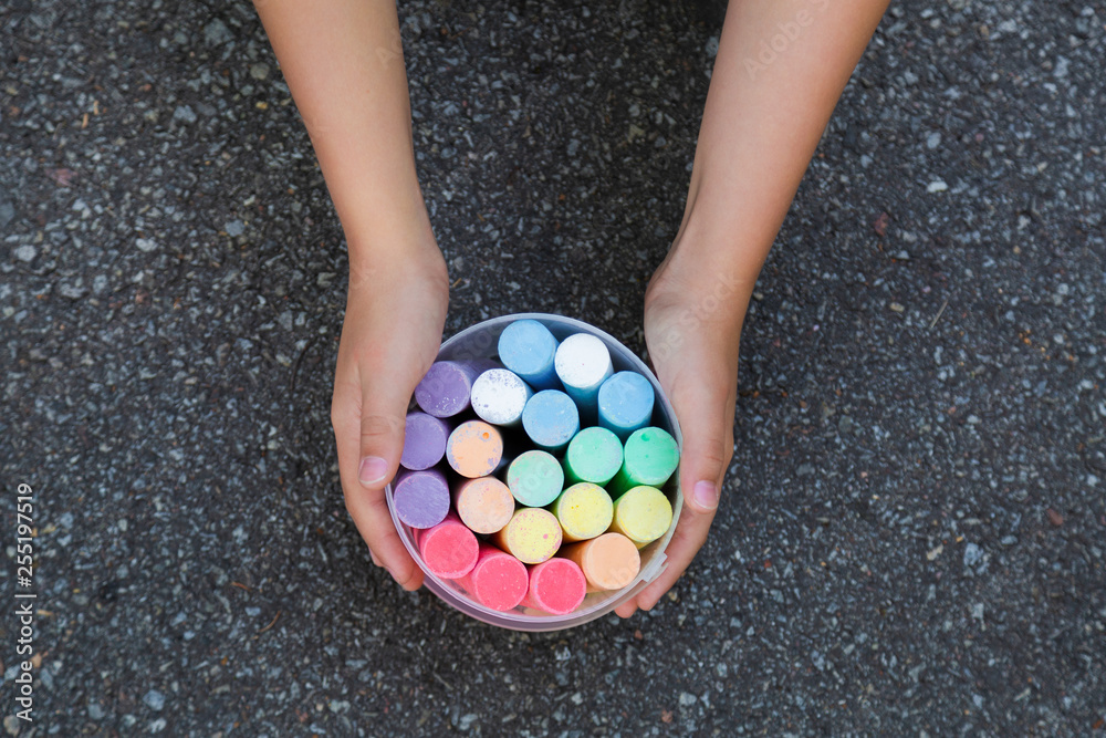 Closeup top view of hands of child going to draw pictures with colorful chalks outdoors using surface of grey grunge pavement as background. Horizontal color photography. Closeup top view of hands of child going to draw pictures with colorful chalks outdoors using surface of grey grunge pavement as background. Horizontal color photography.