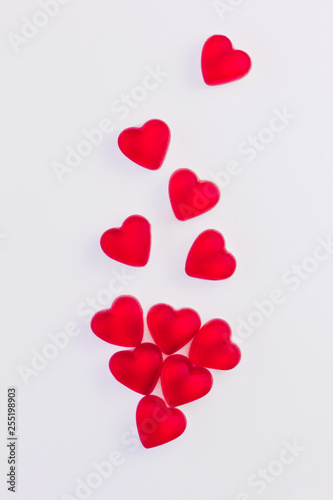 Concept of falling hearts made of heart shaped red jelly sweets on isolated white background. Top view.
