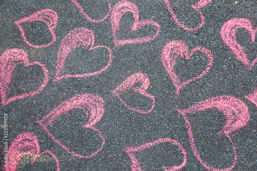 Drawing of many pink hearts with chalk on grey sidewalk. Horizontal color photography.