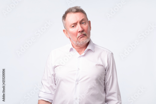 Old senior man in white shirt with serious and sad expression.