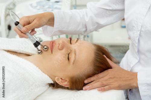 Close up shot of a professional cosmetologist performing stimulating facial treatment for her female client. Beautiful woman getting microcurrent facials at spa salon skincare electrodes apparatus