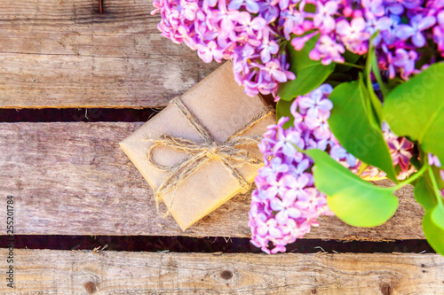 Floral decor elements. Small gift box with presents wrapped craft brown paper with bouquet of flowers beautiful smell violet purple lilac in vase on rustic wooden background. Copy space