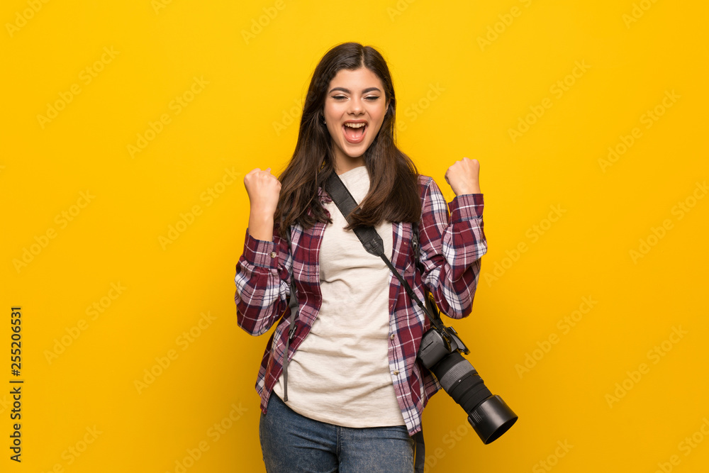 Photographer teenager girl over yellow wall celebrating a victory in winner position Photographer teenager girl over yellow wall celebrating a victory in winner position