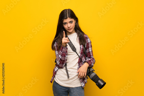 Photographer teenager girl over yellow wall frustrated and pointing to the front