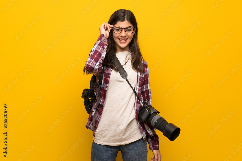 Photographer teenager girl over yellow wall with glasses and surprised Photographer teenager girl over yellow wall with glasses and surprised