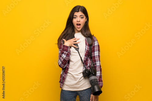 Photographer teenager girl over yellow wall surprised and shocked while looking right © luismolinero