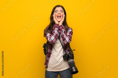 Photographer teenager girl over yellow wall shouting and announcing something © luismolinero