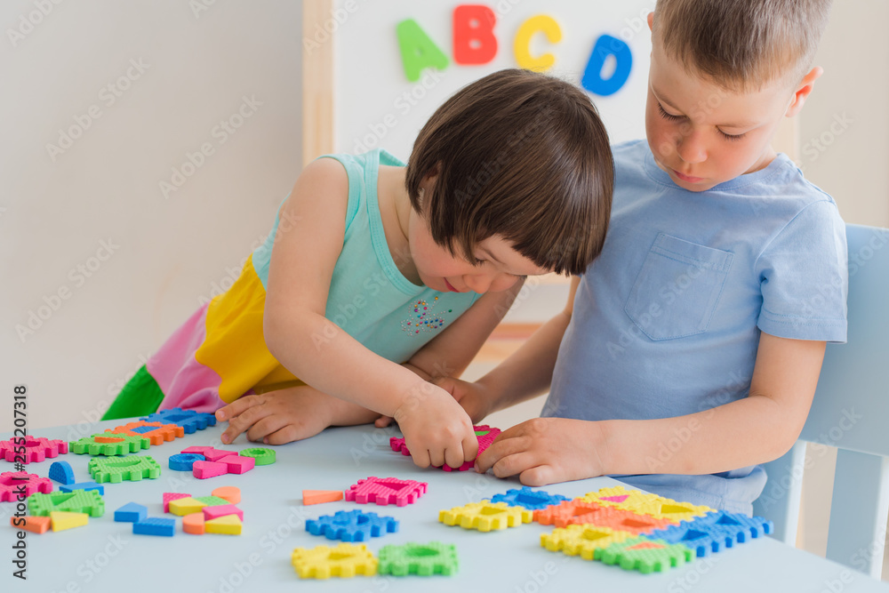 Fototapeta premium A boy and a girl collect a soft puzzle at the table. Brother and sister have fun playing together in the room.