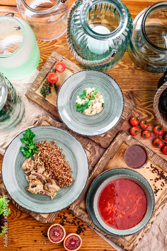 National Russian and Ukrainian dishes: borscht, buckwheat with stewed mushrooms and Russian salad in gray plates on wooden boards in rustic composition. close-up. top view