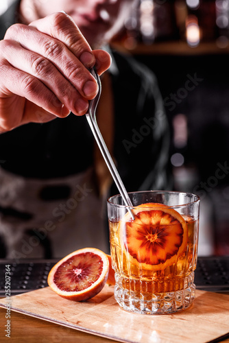Bartender does beautiful cocktail with Sicilian orange in a transparent glass on the bar.space. close up