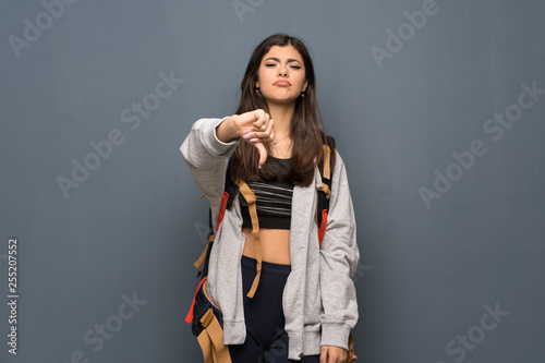 Teenager traveler girl over wall showing thumb down with negative expression