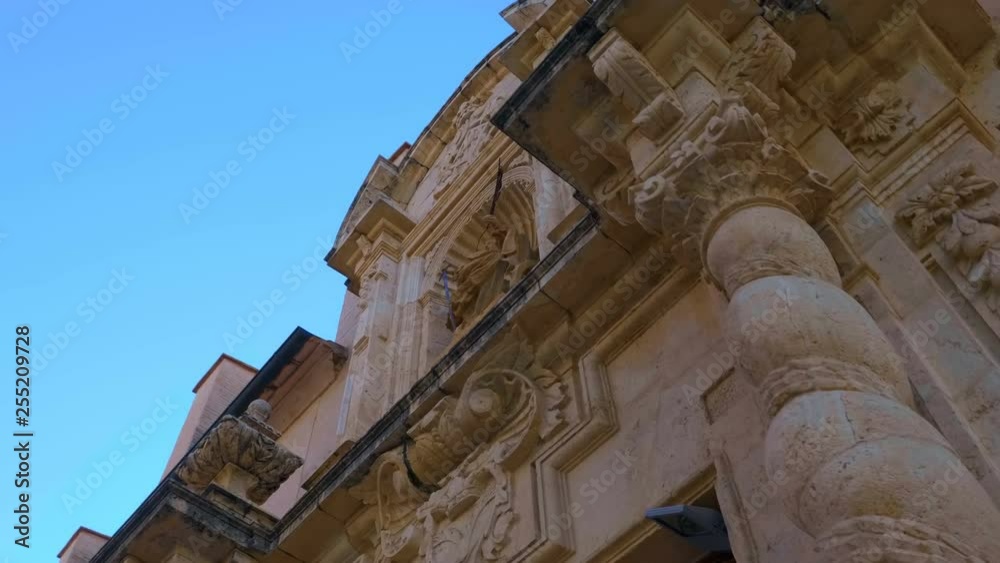 Beautiful ancient church with twisted columns, a ornate decorated facade and a statue of the saint above the entrance, in the Spain city against the blue sky. There is also a belfry with bells in the Beautiful ancient church with twisted columns, a ornate decorated facade and a statue of the saint above the entrance, in the Spain city against the blue sky. There is also a belfry with bells in the