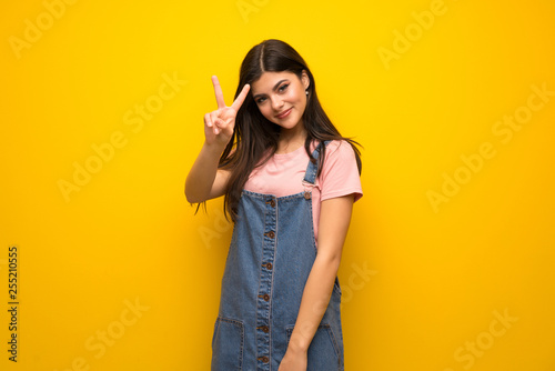 Teenager girl over yellow wall smiling and showing victory sign