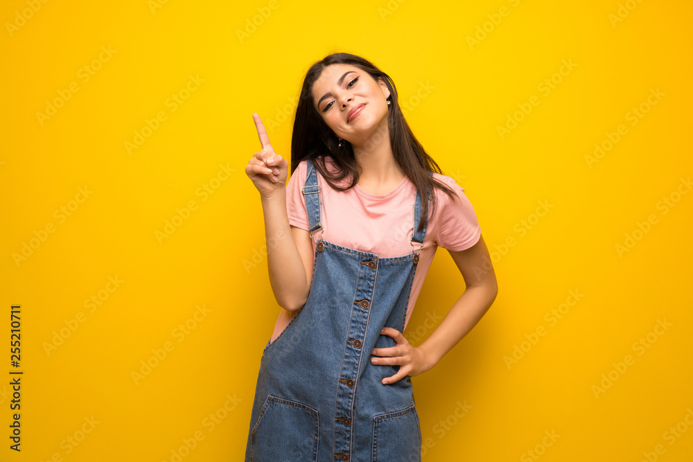 Teenager girl over yellow wall showing and lifting a finger in sign of the best Teenager girl over yellow wall showing and lifting a finger in sign of the best