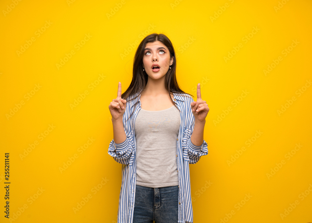 Teenager girl over yellow wall pointing up and surprised Teenager girl over yellow wall pointing up and surprised