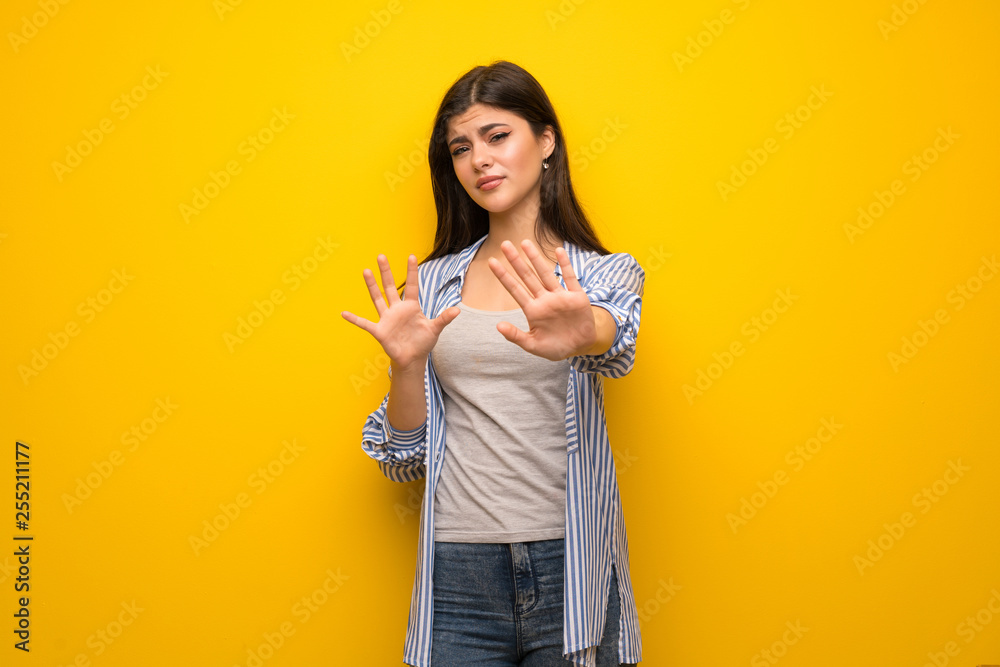Teenager girl over yellow wall nervous and scared stretching hands to the front Teenager girl over yellow wall nervous and scared stretching hands to the front