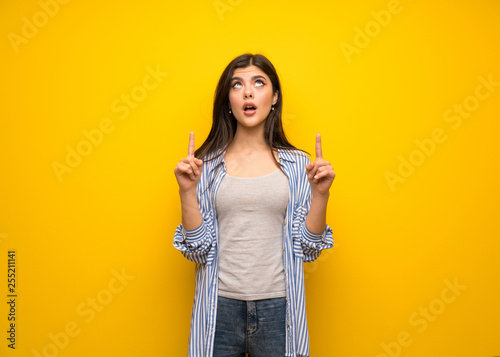 Teenager girl over yellow wall pointing up and surprised