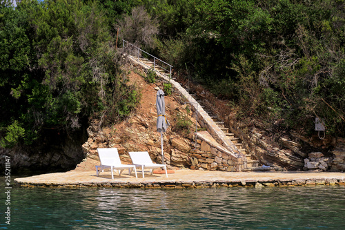 Private beaches on mediterranean sea. Chairs, deck chairs, sun loungers and parasols waiting for tourists. Tiny secluded rocky beach with lush vegetation of olive trees and swimming area at ocean. © zoranlino